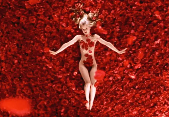 Una donna giace su un letto di rose rosse, un'immagine iconica che evoca la bellezza e la complessità di "American Beauty recensione".