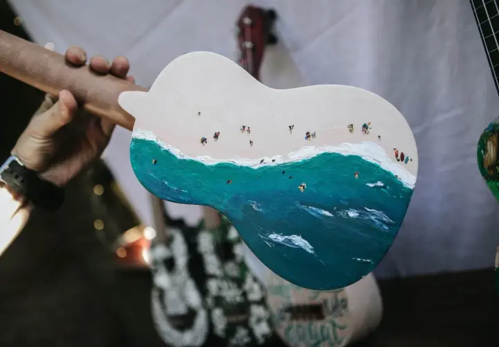 Un ukulélé peint d'une scène de plage animée. La taille ukulele est parfaite pour emporter cette œuvre d'art en voyage.