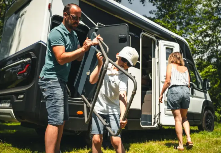Un père et son fils sortent une chaise pliante de leur camping-car, prêts pour une aventure en Ardeche.