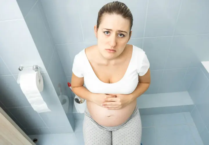 Femme enceinte au premier trimestre, le visage marqué par l'inconfort, se tenant le ventre. La constipation grossesse 1er trimestre est une réalité pour beaucoup.