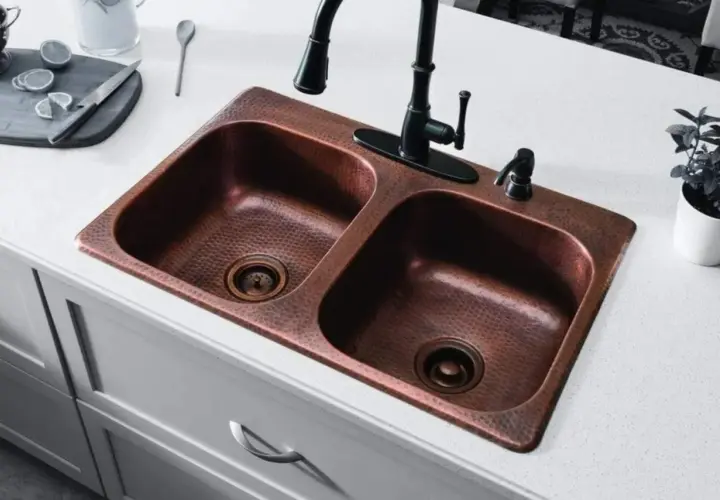 Fregadero doble de cobre martillado con grifo negro. Un truco para limpiar cobre con vinagre es ideal para mantenerlo brillante.