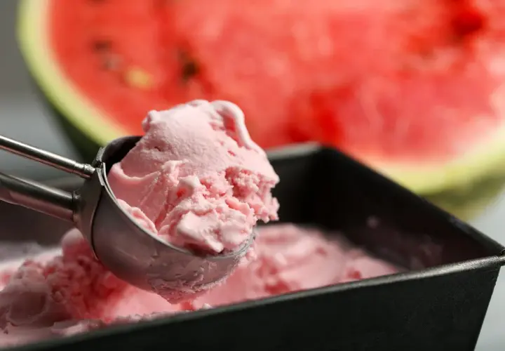 Un cucchiaio raccoglie una pallina di cremoso gelato anguria fatto in casa, con una fetta di anguria sullo sfondo.