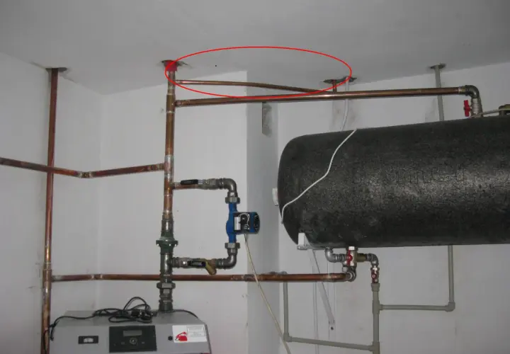 Instalacja hydrauliczna z bojlerem i pompą obiegową. Pokazano fragment instalacji, jak podłączyć zawór bezpieczeństwa do bojlera, z widocznymi rurami miedzianymi i złączkami.