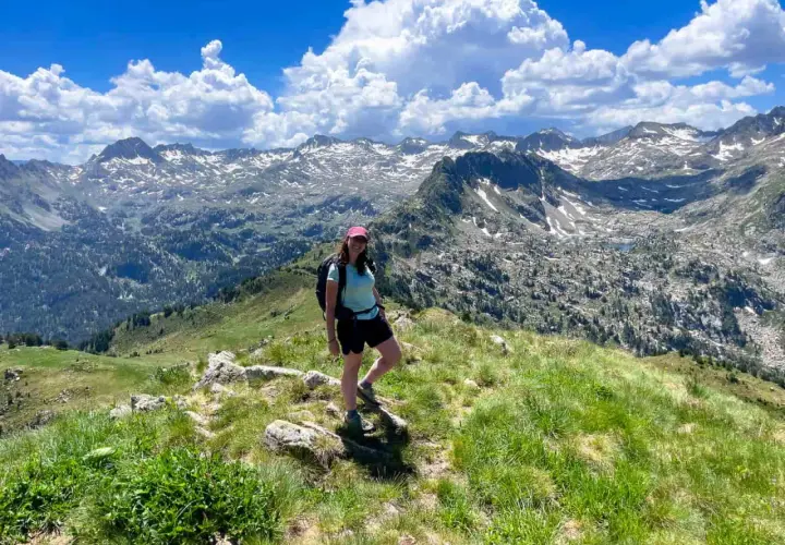 Senderista disfruta de las impresionantes vistas de las rutas del Valle de Arán, con picos nevados y un cielo azul con nubes.