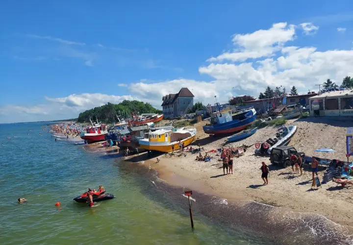 Słoneczne **morze bałtyckie wakacje** z kolorowymi łodziami na plaży i tłumem ludzi cieszących się słońcem.