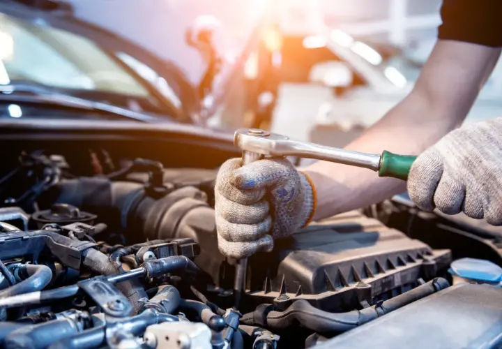 Mechanik w rękawicach dokręca śrubę kluczem nasadowym w silniku samochodu. Może to być naprawa po problemach po płukance silnika.