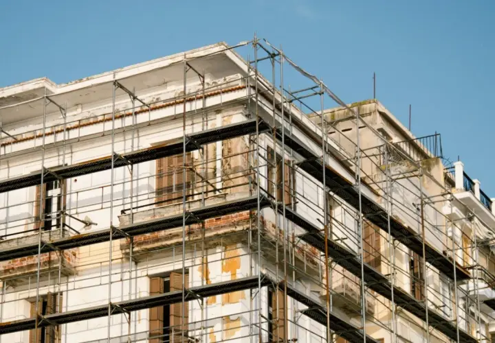 Bâtiment en rénovation, échafaudages pour aide ravalement façade sans isolation extérieur. Le ciel est bleu.
