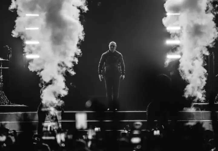 Pitbull na scenie, otoczony dymem i światłami, podczas koncertu.