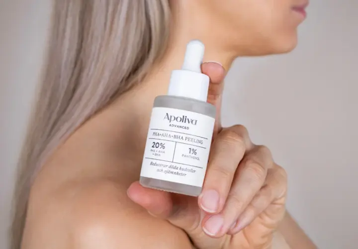 En kvinna håller en flaska med Apoliva PHA+AHA+BHA PEELING. Denna aha syra-produkt hjälper till att reducera döda hudceller.