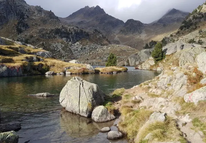 Paisaje sereno en el Vall d'Ora Gorgs, con un lago de aguas cristalinas rodeado de rocas y montañas escarpadas.