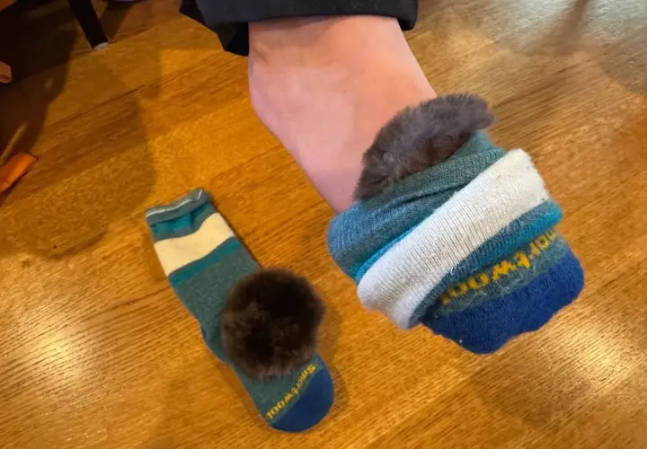 A foot wearing a fluffy-lined sock, with another striped sock and pom-pom nearby. Perfect for learning how to keep feet warm in boots.