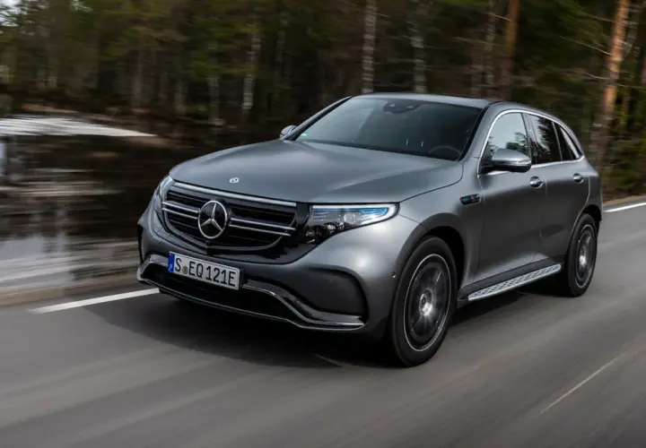 Szary Mercedes EQC jedzie po drodze wśród drzew.