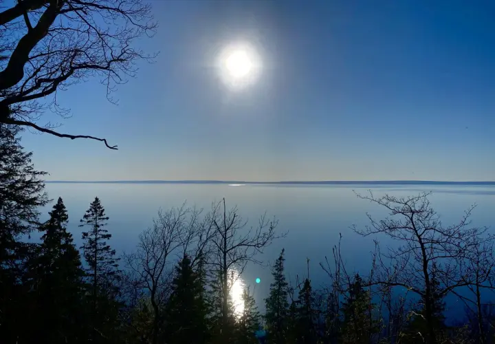 En solig dag för omberg vandring. Träd silhuetter mot en klarblå himmel och ett glittrande vatten.