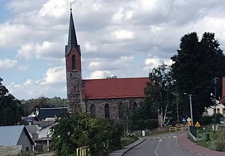 Kamienny kościół z czerwoną dachem i strzelistą wieżą to jedna z głównych atrakcji Sierakowic. Wokół widać domy i zieleń.