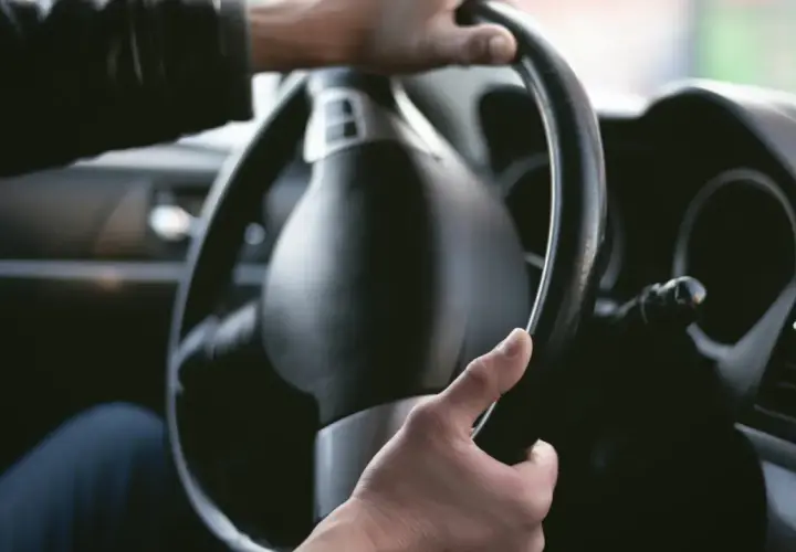 Manos sujetando el volante de un coche. La dirección del coche rota, indicando un giro o una maniobra.