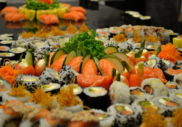 Mnóstwo sushi z łososiem, ogórkiem i sałatą. Wśród nich widać kawałki ryby maślanej, tworząc apetyczną kompozycję.