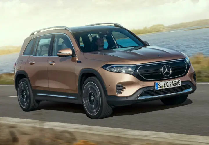 Brązowy Mercedes EQB jedzie po drodze nad jeziorem.