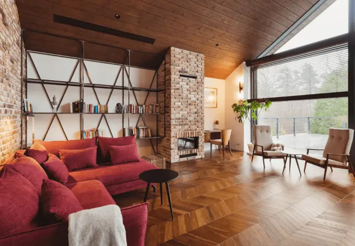 Przytulny salon w stylu wiejskim z ceglanym kominkiem, czerwoną kanapą i drewnianą podłogą.