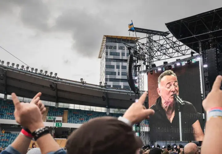 Publiken njuter av en Bruce Springsteen konsert i Sverige. En storbildsskärm visar The Boss sjunga medan fansen gestikulerar.