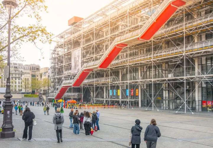 Widok na Centre Pompidou z czerwonymi schodami ruchomymi i ludźmi spacerującymi po placu.