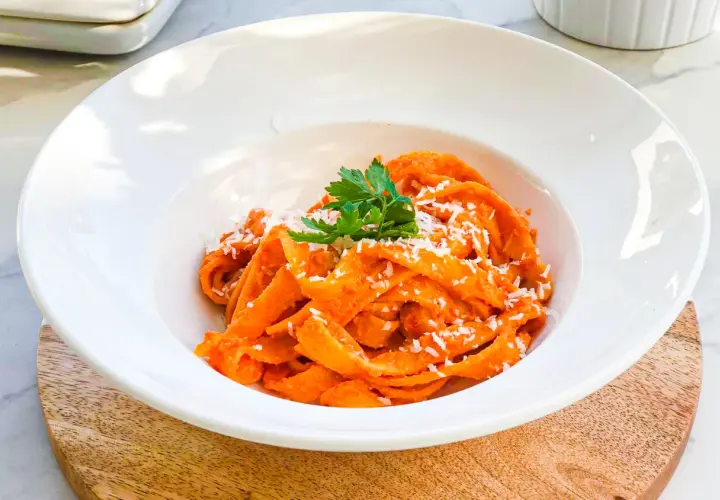 Pappardelle z kremowym sosem z pieczonej papryki, posypane parmezanem i udekorowane natką pietruszki. Pyszne danie, które zachwyca smakiem.