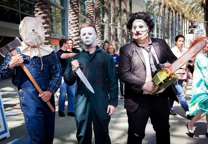 Trzech mężczyzn w strojach znanych postaci z horrorów: jeden z workiem na głowie i siekierą, drugi jako Michael Myers z nożem, trzeci jako Leatherface z piłą łańcuchową. Groźny slasher na konwencie.