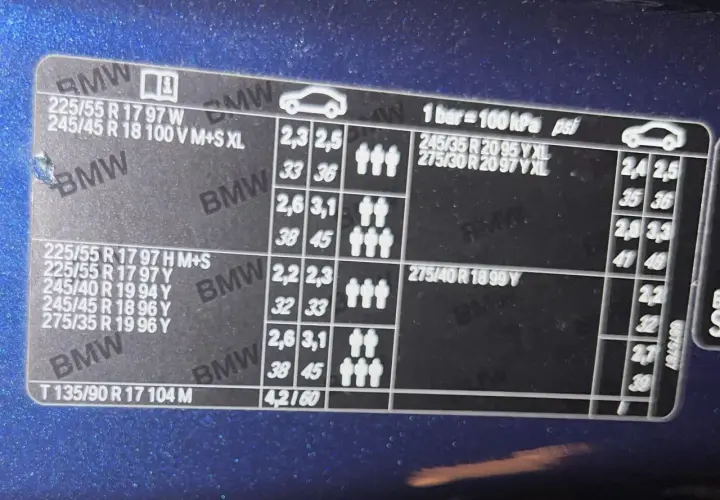 Naklejka BMW z informacją o ciśnieniu w oponach. Dla rozmiaru 225/55 R17, ciśnienie wynosi 2,3-2,5 bar (33-36 psi) przy obciążeniu do 3 osób.