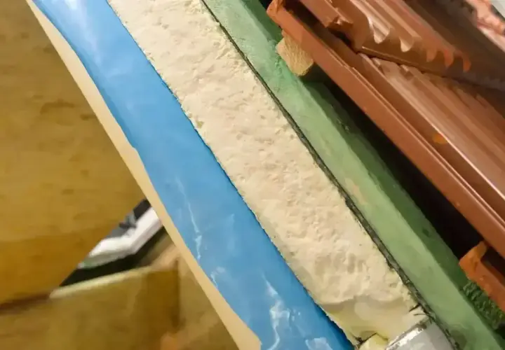 Warstwa izolacyjna z materiału pu w przekroju dachu, widoczna pianka, folia niebieska i dachówka.