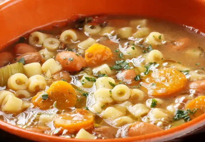 Gęsta, aromatyczna zupa minestrone z makaronem, fasolą, marchewką i ziemniakami, posypana natką pietruszki.