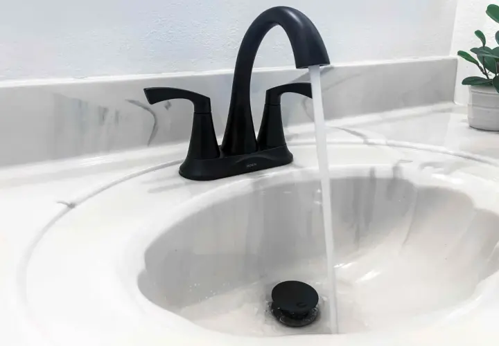 Rubinetto nero moderno in un lavandino bianco, con acqua che scorre. Uno stilema fad che aggiunge un tocco di eleganza.