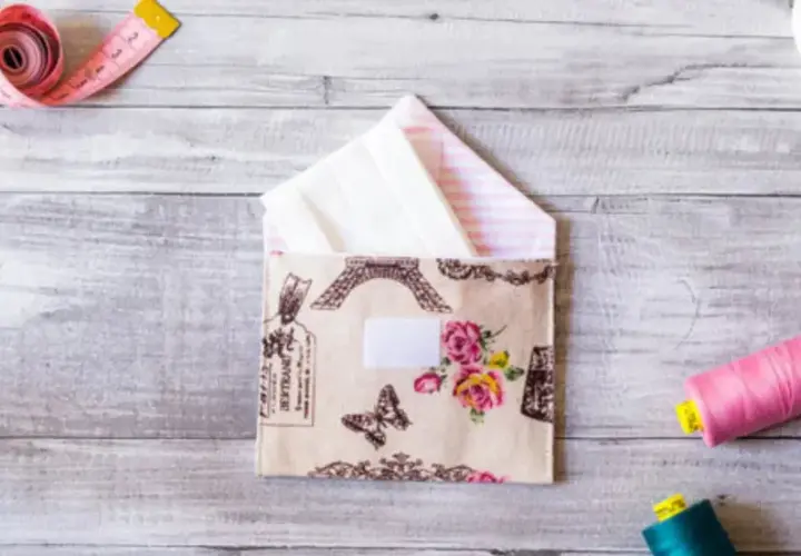 Sobres de tela con diseño de París y flores, junto a carretes de hilo, cinta métrica y descosedor.