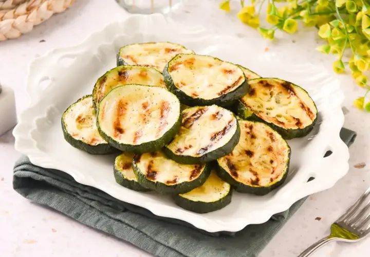 Rodajas de calabacín a la plancha, con marcas de parrilla doradas, servidas en un plato blanco festoneado.
