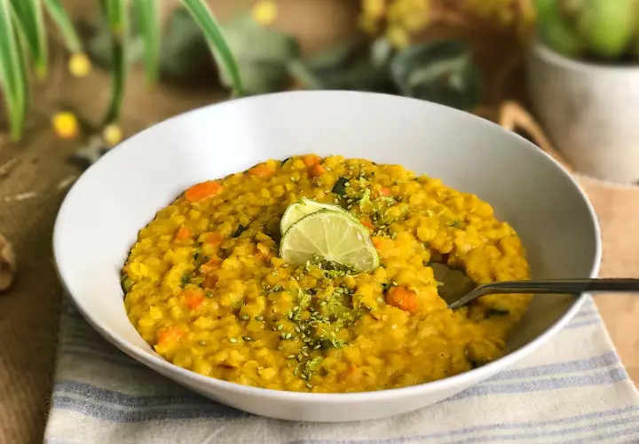 Un tazón de lentejas al curry con zanahoria y calabacín, decorado con rodajas de lima y ralladura.