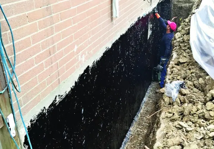 Pracownik nakłada czarną hydroizolację na ścianę fundamentową.
