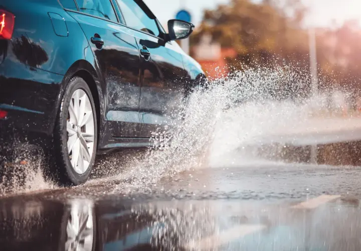 Coche negro salpicando agua. Para evitar el aquaplaning, reduce la velocidad y mantén tus neumáticos en buen estado.