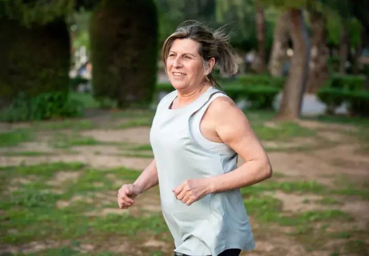 Uśmiechnięta kobieta w średnim wieku cieszy się bieganiem 5 km dziennie w parku.