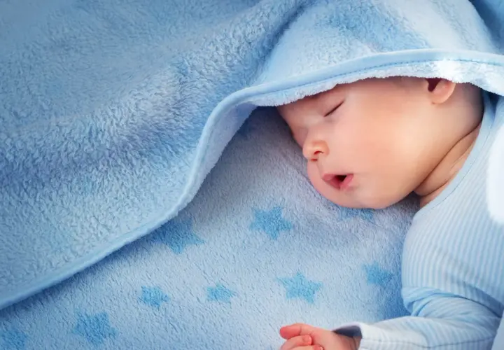 Sover gott under ett mjukt, blått täcke med stjärnor. Liten bebis svettas lite i sömnen.