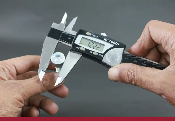 Manos sujetan un tornillo hexagonal y un calibre digital para su calibre medicion. La pantalla muestra 1.222.