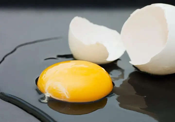 Rozbite jajko na ciemnym tle. Żółtko lśni, a skorupka czeka na usmażenie. Zastanawiasz się nad jajko smażone kcal?