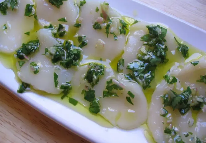 Délicieux carpaccio de saint jacques crues, nappé d'une vinaigrette aux herbes fraîches et à l'ail. Un plat léger et savoureux.