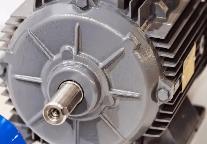 Dettaglio di un motore elettrico grigio, con albero motore visibile e una targhetta dorata.