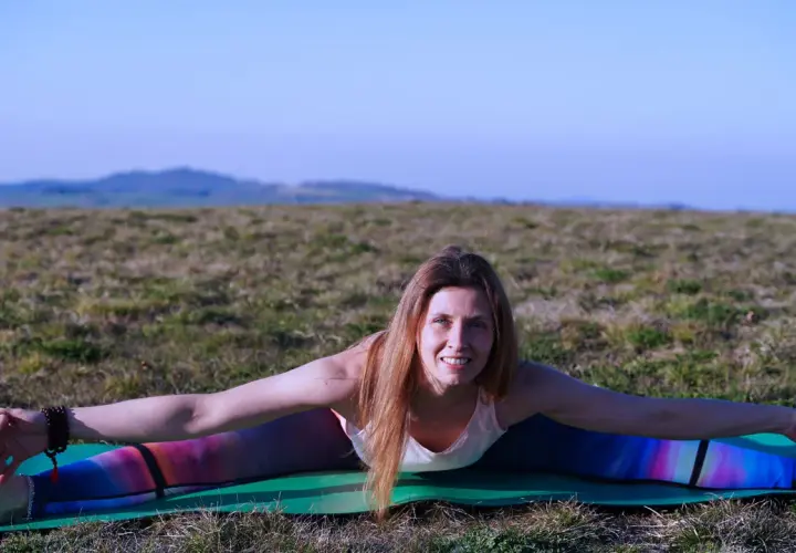 Donna in posa yoga all'aperto, con le gambe divaricate, che lavora sul primo chakra sessualità.
