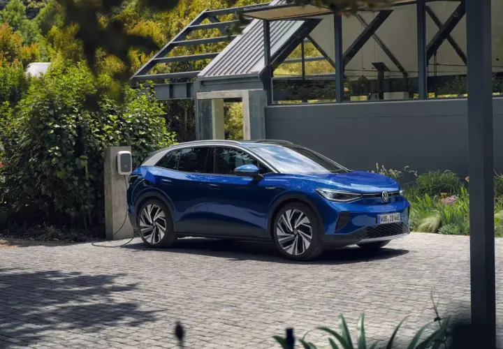 Niebieski VW ID.4 ładuje się przy nowoczesnym domu. Elektryczny SUV stoi na podjeździe, podłączony do ładowarki.