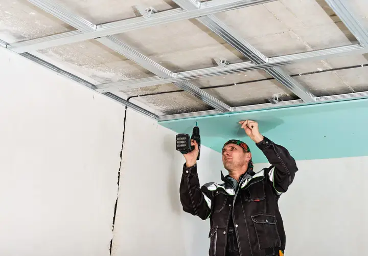 Un ouvrier installe une plaque de plâtre sur une structure métallique, créant ainsi un plafond technique.