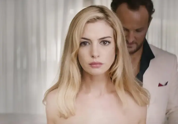 Anne Hathaway, protagonista de "L'isola dell'inganno", con uno sguardo intenso. Dietro di lei, un uomo in giacca bianca.