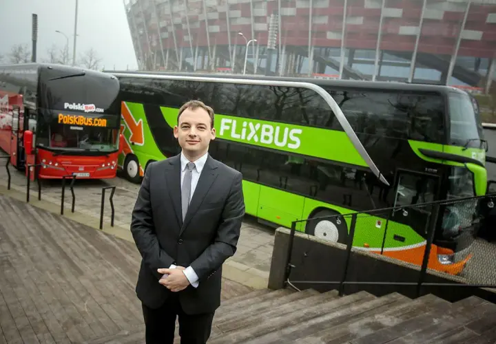 Mężczyzna w garniturze stoi przed zielonym autokarem Flixbus i czerwonym autokarem Polskibus.