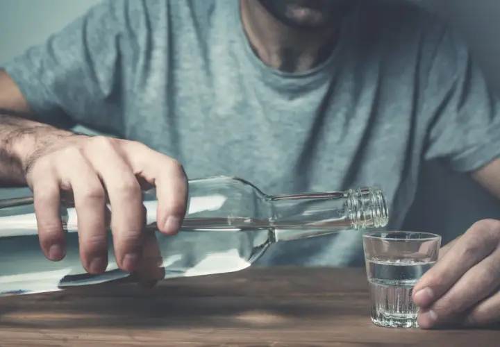Mężczyzna nalewa alkohol do kieliszka. To może być jeden z objawów przed śmiercią alkoholika, symbol jego walki.