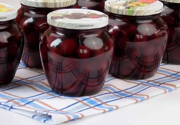 Słoiki pełne kompotu z czereśni, gotowe na zimę. Ciemne owoce w słodkim syropie kuszą smakiem.