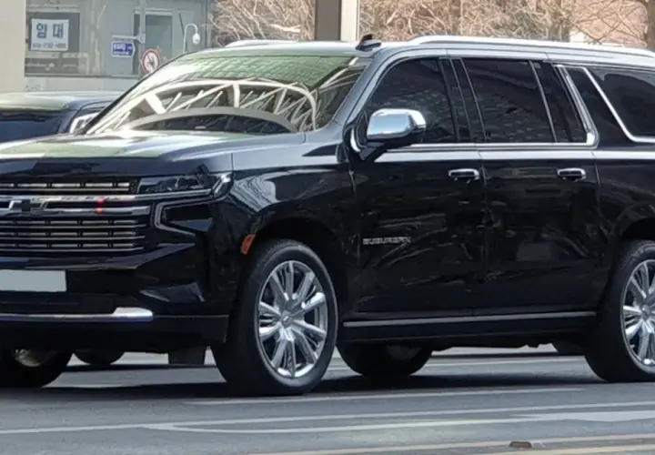 Czarny Chevrolet Suburban, który wygląda jak największe auto na świecie, z chromowanymi felgami i błyszczącą atrapą chłodnicy.
