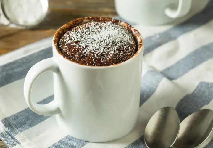 Un delizioso mug cake al cioccolato, spolverato di zucchero a velo, pronto per essere gustato.